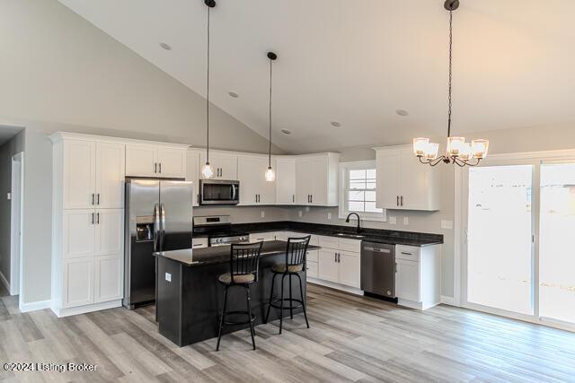 kitchen featuring high vaulted ceiling, decorative light fixtures, a kitchen island, white cabinetry, and stainless steel appliances