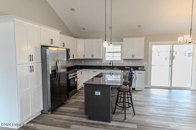 kitchen with stainless steel appliances, a kitchen island, vaulted ceiling, a breakfast bar, and white cabinets