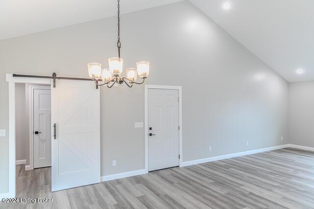 spare room featuring a barn door, high vaulted ceiling, light hardwood / wood-style flooring, and a notable chandelier