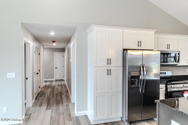 kitchen with lofted ceiling, light hardwood / wood-style flooring, dark stone countertops, white cabinetry, and stainless steel appliances