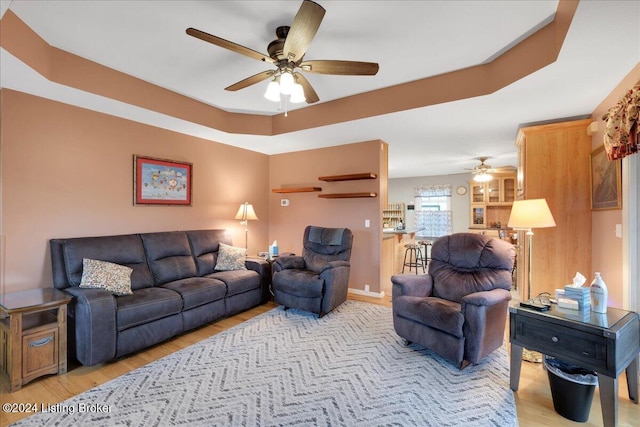 living room featuring light wood-type flooring, a tray ceiling, and ceiling fan