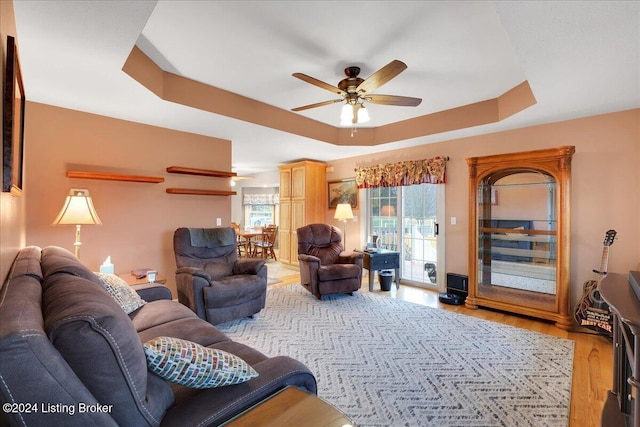 living room featuring ceiling fan, light hardwood / wood-style floors, and a tray ceiling