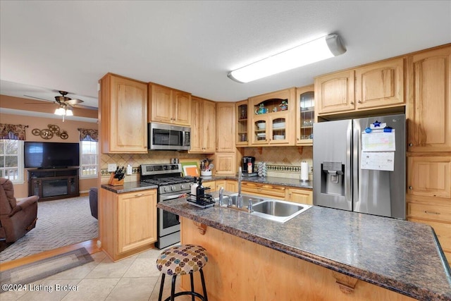 kitchen featuring backsplash, a kitchen breakfast bar, sink, ceiling fan, and stainless steel appliances