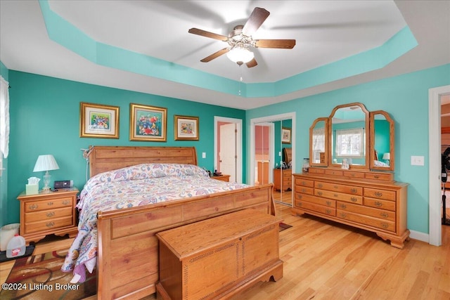 bedroom with light hardwood / wood-style floors, a raised ceiling, and ceiling fan