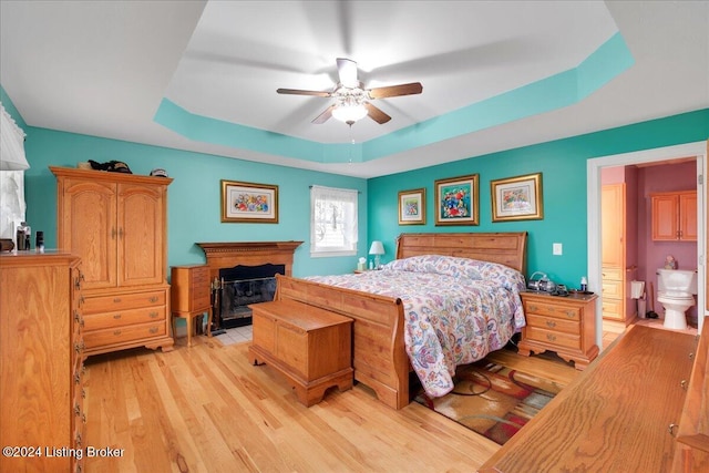 bedroom with ceiling fan, a raised ceiling, light hardwood / wood-style flooring, and ensuite bath