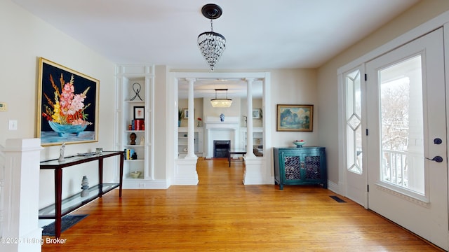 foyer with decorative columns, a healthy amount of sunlight, light wood-type flooring, and an inviting chandelier