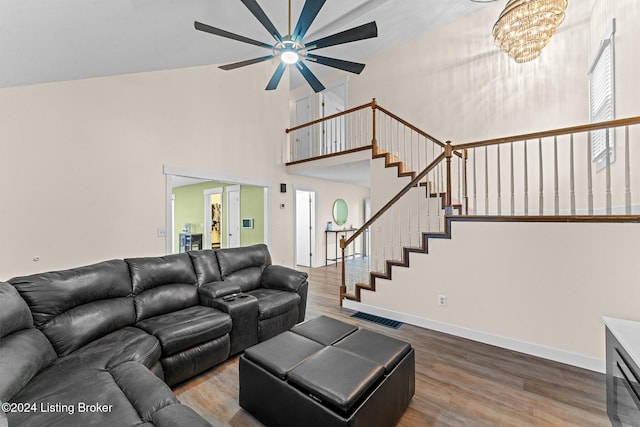 living room with ceiling fan with notable chandelier, a healthy amount of sunlight, wood-type flooring, and high vaulted ceiling