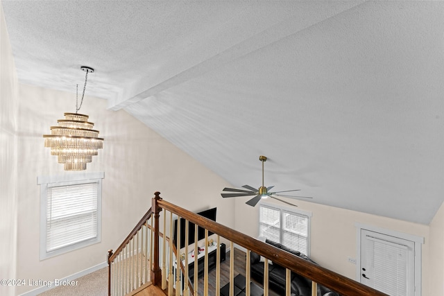 stairs featuring ceiling fan with notable chandelier, a textured ceiling, and lofted ceiling with beams