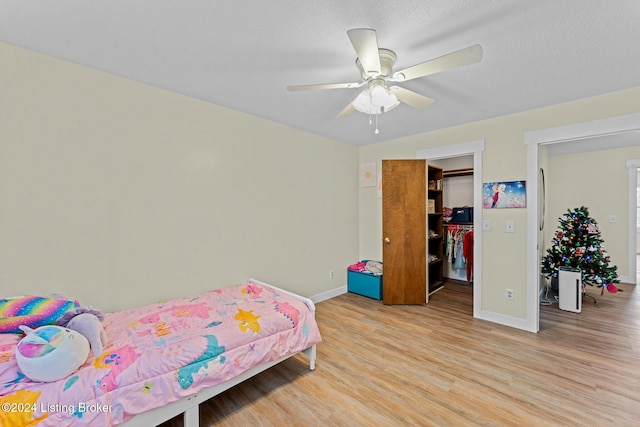 bedroom featuring ceiling fan, light hardwood / wood-style floors, a walk in closet, and a textured ceiling