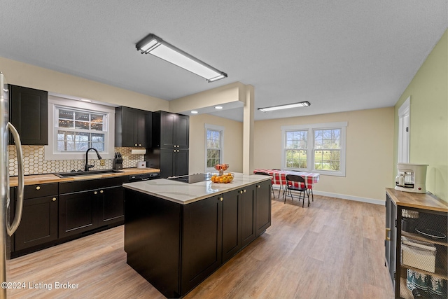 kitchen with tasteful backsplash, black electric cooktop, sink, light hardwood / wood-style flooring, and a center island