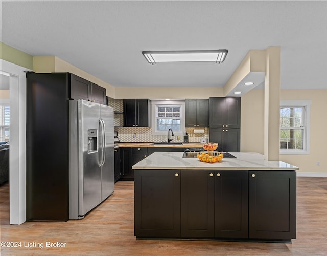 kitchen with stainless steel fridge, light wood-type flooring, light stone countertops, and sink