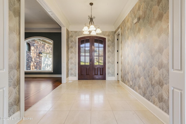 foyer with plenty of natural light, an inviting chandelier, crown molding, and french doors