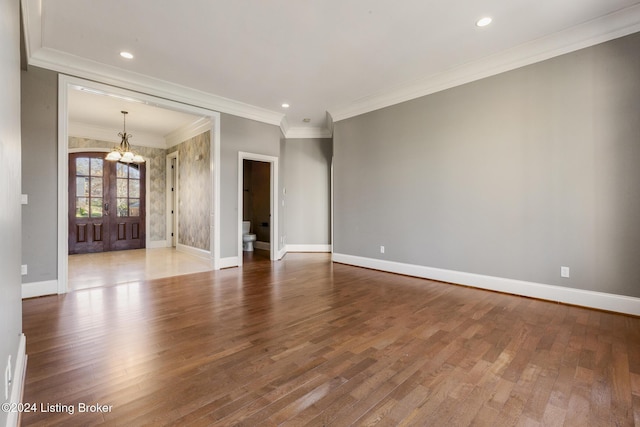 empty room with a chandelier, wood-type flooring, french doors, and ornamental molding