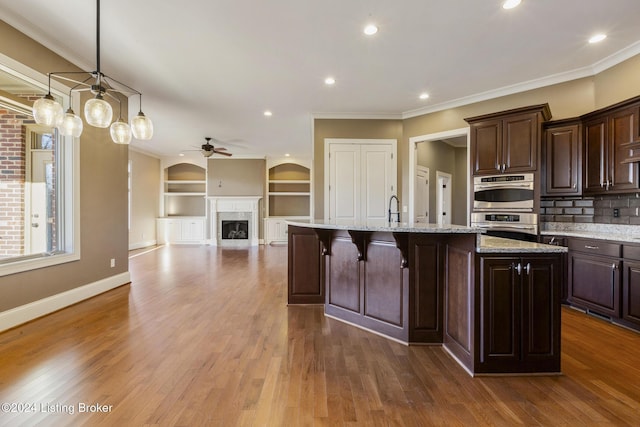 kitchen with dark brown cabinets, dark hardwood / wood-style flooring, ceiling fan, and an island with sink