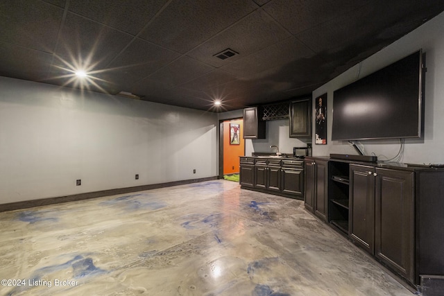 interior space with dark brown cabinets, concrete floors, a drop ceiling, and sink