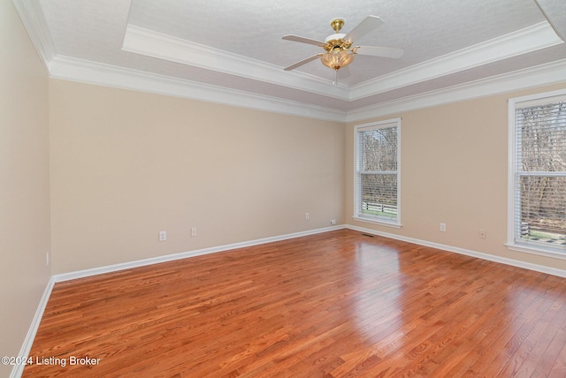 empty room with ceiling fan, wood-type flooring, ornamental molding, and a tray ceiling