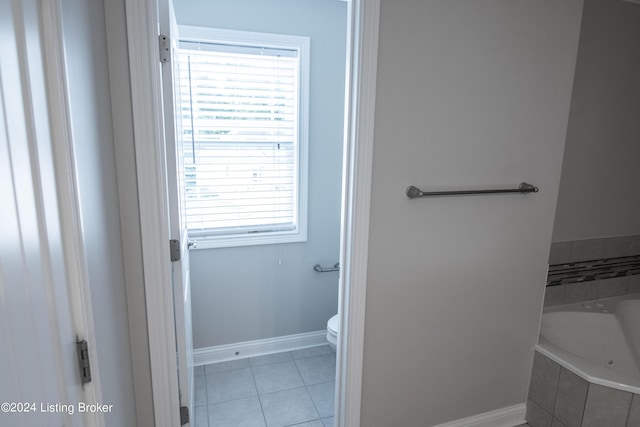 bathroom featuring tile patterned flooring, tiled bath, and toilet