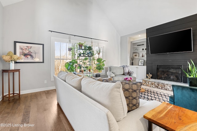 living room featuring high vaulted ceiling, dark hardwood / wood-style flooring, a large fireplace, and built in features