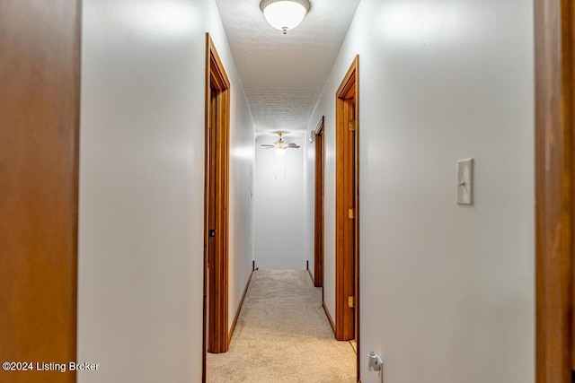 corridor with light colored carpet and a textured ceiling