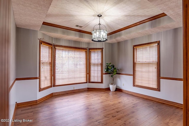 spare room featuring a textured ceiling, ornamental molding, a raised ceiling, a notable chandelier, and hardwood / wood-style flooring