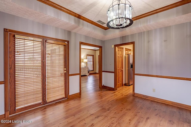 unfurnished dining area with an inviting chandelier, ornamental molding, light hardwood / wood-style floors, and a textured ceiling