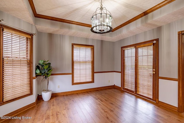 unfurnished room with a textured ceiling, ornamental molding, a tray ceiling, a notable chandelier, and light hardwood / wood-style floors