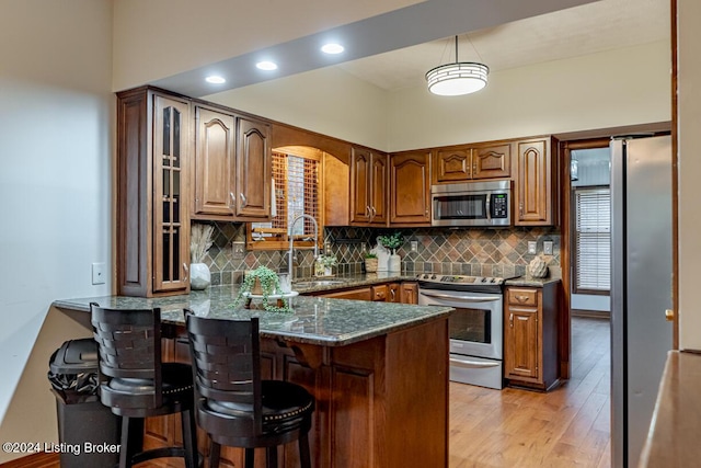 kitchen featuring appliances with stainless steel finishes, a breakfast bar, sink, dark stone counters, and kitchen peninsula