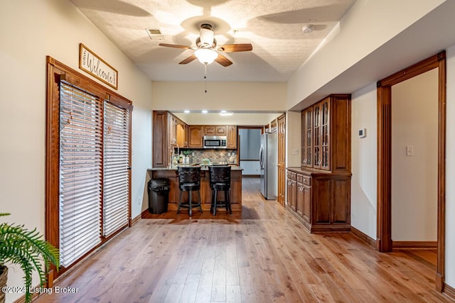 kitchen with a kitchen island, appliances with stainless steel finishes, a breakfast bar, backsplash, and light hardwood / wood-style flooring