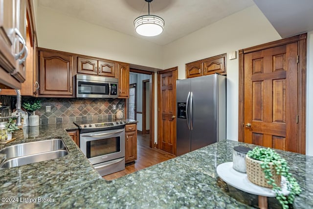 kitchen featuring dark stone countertops, backsplash, wood-type flooring, and stainless steel appliances