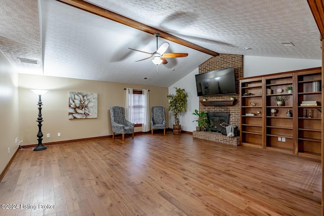 unfurnished room featuring a fireplace, lofted ceiling with beams, wood-type flooring, ceiling fan, and a textured ceiling