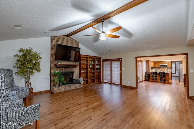 living room featuring a brick fireplace, wood-type flooring, lofted ceiling with beams, and a textured ceiling