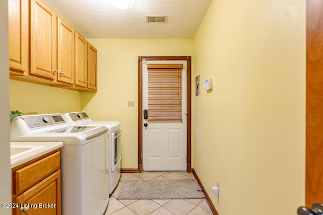 washroom with cabinets, washing machine and dryer, light tile patterned floors, and a textured ceiling