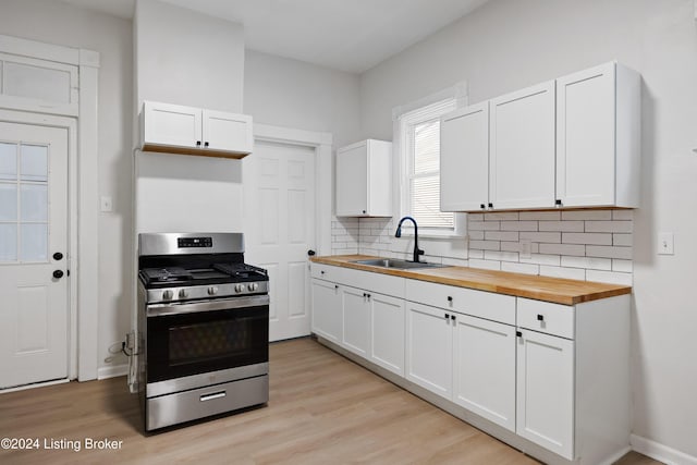 kitchen featuring butcher block counters, backsplash, gas range, light wood-type flooring, and white cabinetry