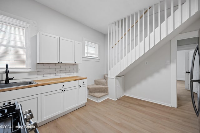 kitchen featuring white cabinets, sink, light wood-type flooring, tasteful backsplash, and butcher block counters