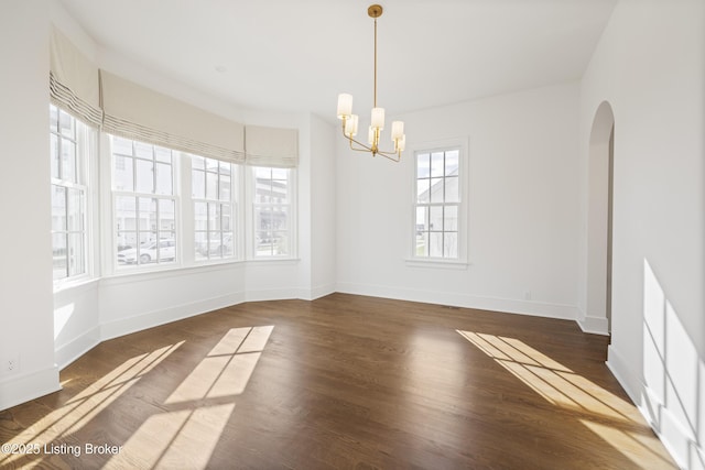 unfurnished room with a notable chandelier, plenty of natural light, and dark wood-type flooring