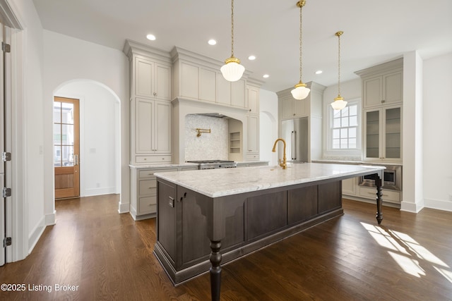 kitchen with tasteful backsplash, light stone counters, high quality fridge, a spacious island, and a breakfast bar area