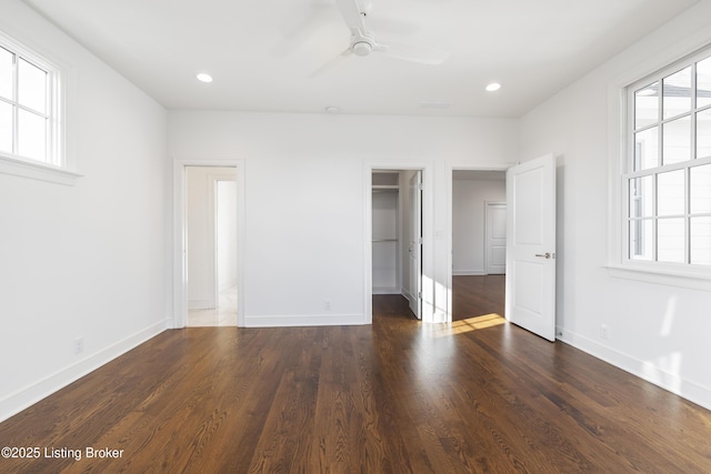 unfurnished bedroom with dark wood-type flooring, ceiling fan, a spacious closet, multiple windows, and a closet