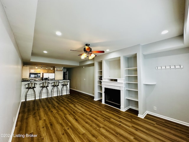 unfurnished living room with built in shelves, dark hardwood / wood-style floors, and ceiling fan