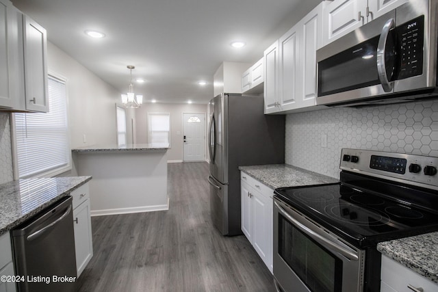 kitchen with appliances with stainless steel finishes, light stone counters, dark wood-type flooring, decorative light fixtures, and white cabinets