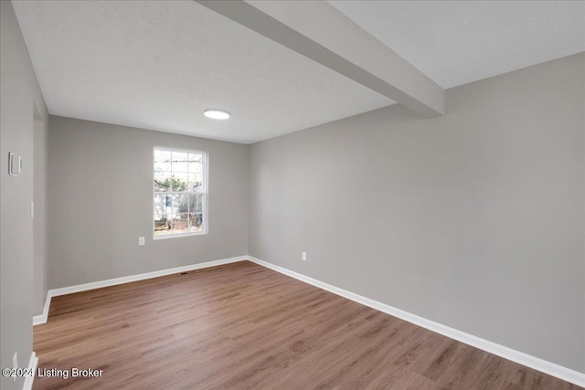 empty room with beam ceiling, a textured ceiling, and hardwood / wood-style flooring