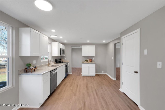 kitchen with light stone countertops, sink, appliances with stainless steel finishes, white cabinets, and light wood-type flooring