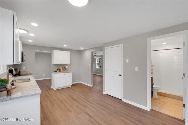 kitchen featuring light hardwood / wood-style floors, light stone countertops, white cabinetry, and sink