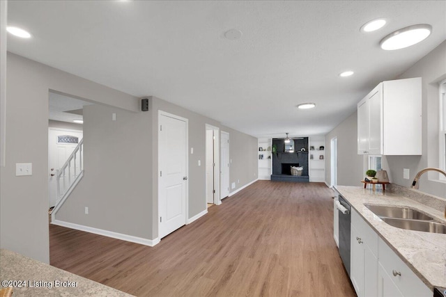 kitchen with sink, light hardwood / wood-style flooring, stainless steel dishwasher, a large fireplace, and white cabinetry