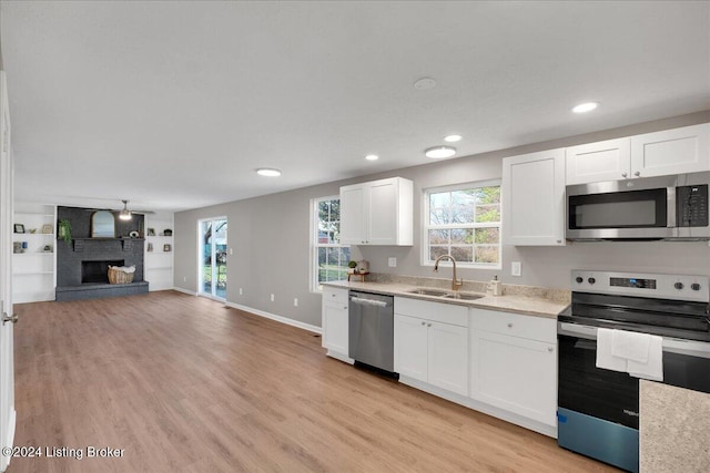 kitchen featuring white cabinetry, sink, stainless steel appliances, light hardwood / wood-style floors, and a fireplace