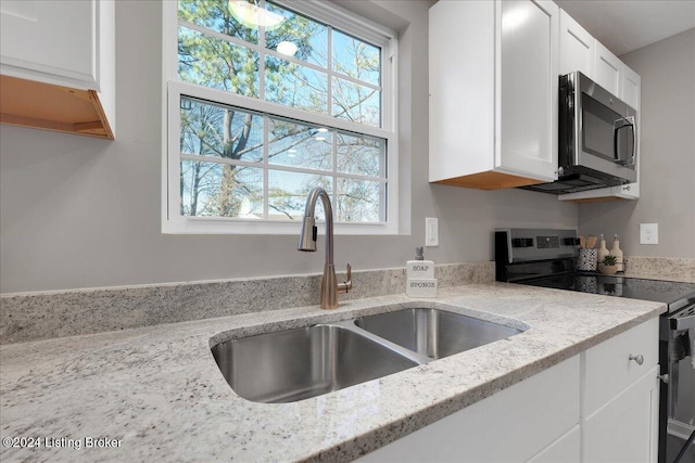 kitchen with stainless steel appliances, light stone counters, white cabinetry, and sink