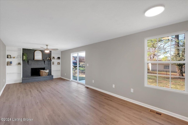 unfurnished living room with hardwood / wood-style floors, plenty of natural light, ceiling fan, and a brick fireplace