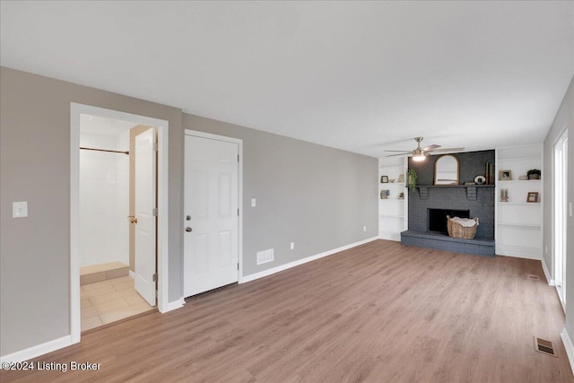 unfurnished living room with a brick fireplace, ceiling fan, built in features, and hardwood / wood-style flooring