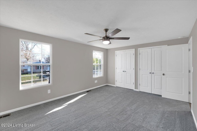 unfurnished bedroom with dark colored carpet, two closets, multiple windows, and ceiling fan