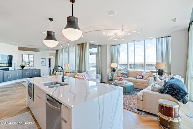 kitchen with light stone countertops, a kitchen island with sink, sink, pendant lighting, and a water view