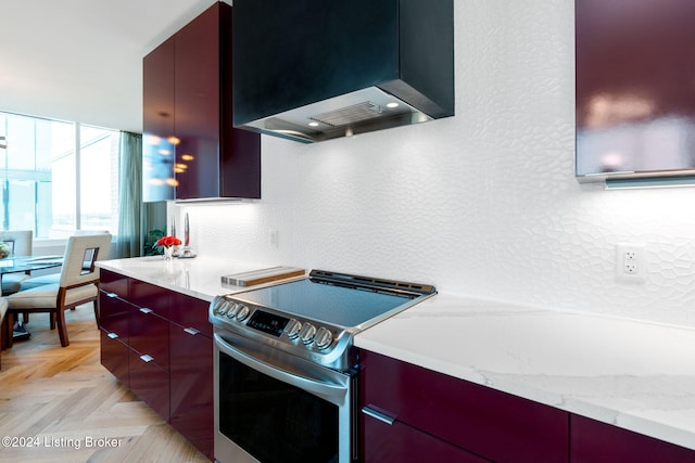 kitchen with wall chimney exhaust hood, light stone countertops, light parquet flooring, and stainless steel range with electric stovetop